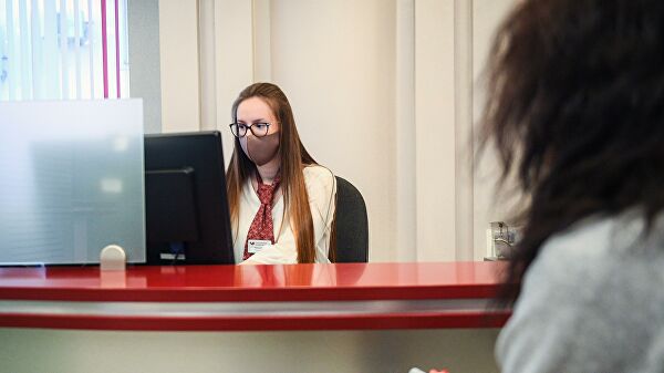 Сотрудница банка в защитной маске ведет прием посетителей в одном из отделений Московского кредитного банка