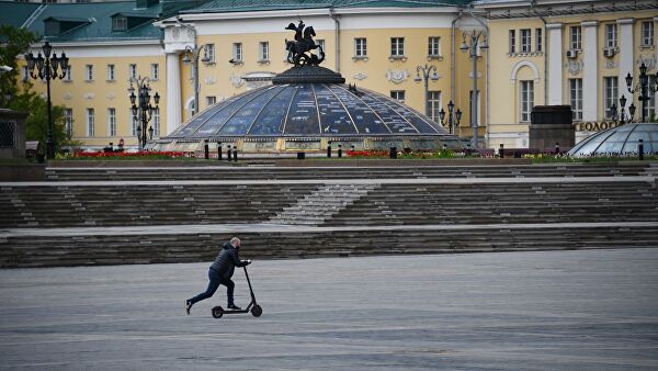 Мужчина едет на электросамокате по Манежной площади в Москве
