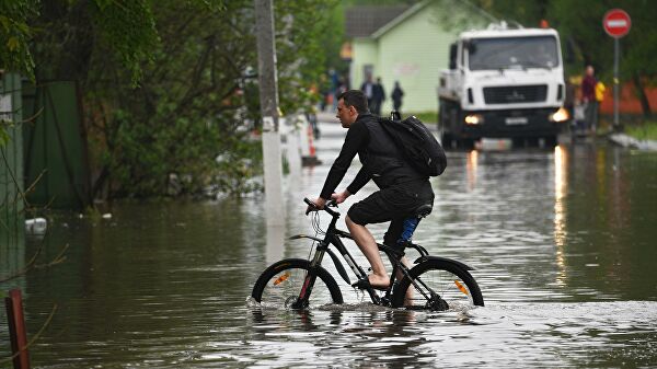 Мужчина на велосипеде на подтопленной улице в поселке Опалиха Московской области
