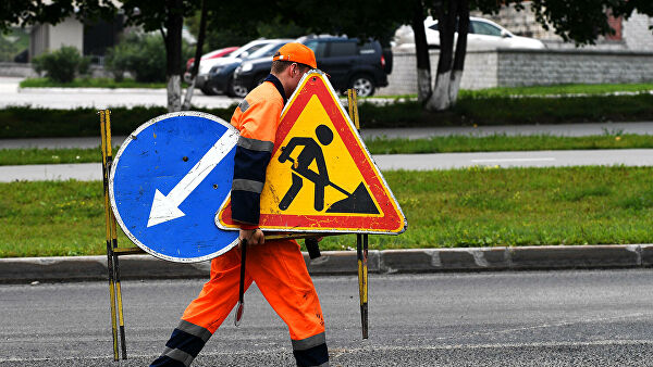 Рабочий переносит дорожные знаки во время укладки верхнего слоя дорожного покрытия
