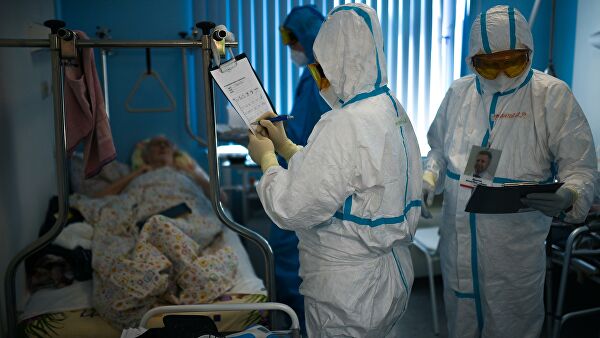 Врачи у постели пациента во время обхода в госпитале для лечения зараженных коронавирусной инфекцией Врачи у постели пациента во время обхода в госпитале для лечения зараженных коронавирусной инфекцией